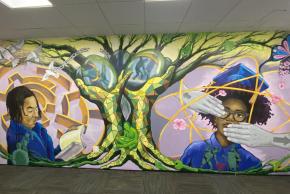 Finished mural featuring portraits of a young man and woman surrounded by symbols of growth, knowledge, and liberation.