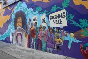 Mural depicting community members marching with signs that read “We are Brownsville.”