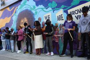 Community members line up in front of the Marcus Garvey Apartments to unveil the new mural.