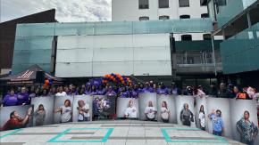 Participants and staff from our RISE program pose outdoors with celebratory photos of survivors at their Survivors Speak event.