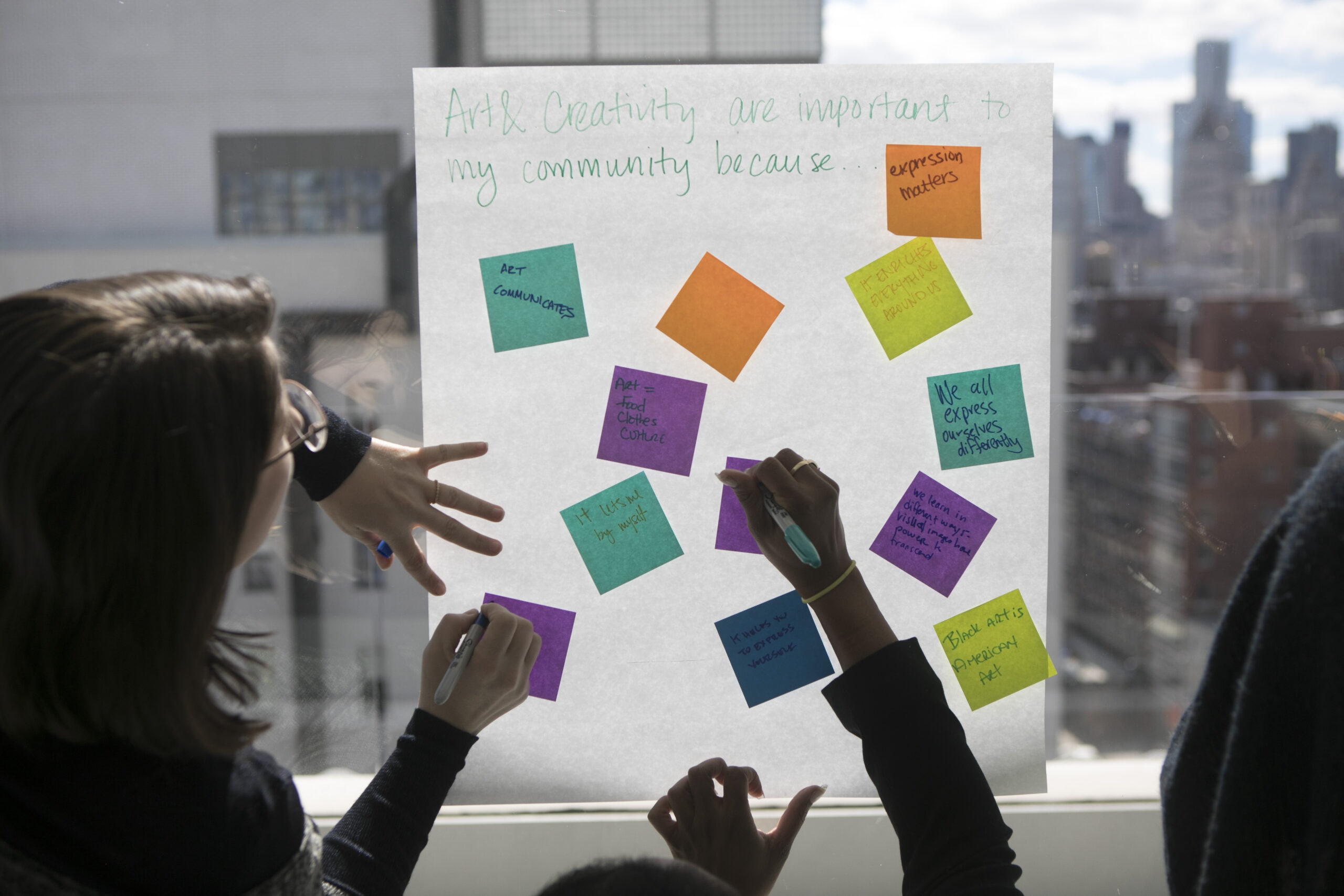 People writing on post-it notes their thoughts on why art and creativity are important to their community. Project Reset group workshop at the New Museum.