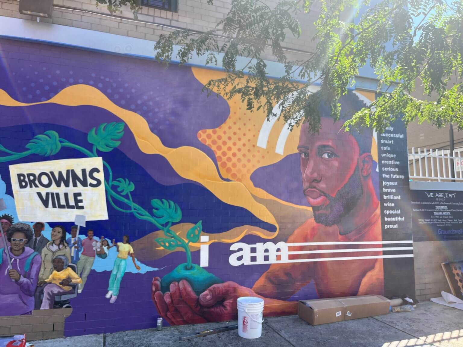 Right side of mural featuring illustration of man holding a patch of soil with long vines growing from it, plus bold text that reads "I am" followed by a list of positive adjectives.