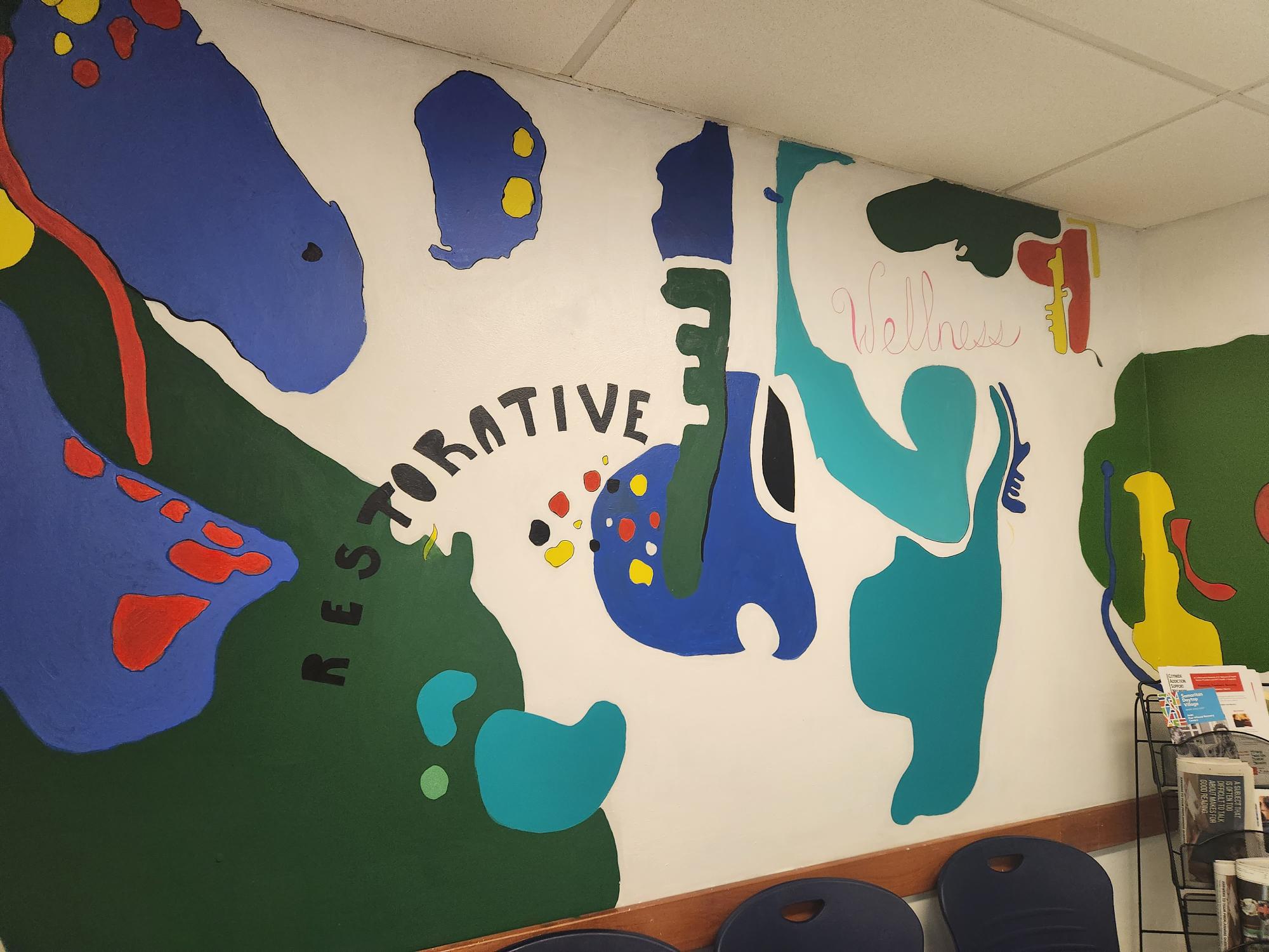 Indoor mural featuring various shapes of blue, red, green, and teal with the words "Restorative" and "Wellness" in decorative font on wall.