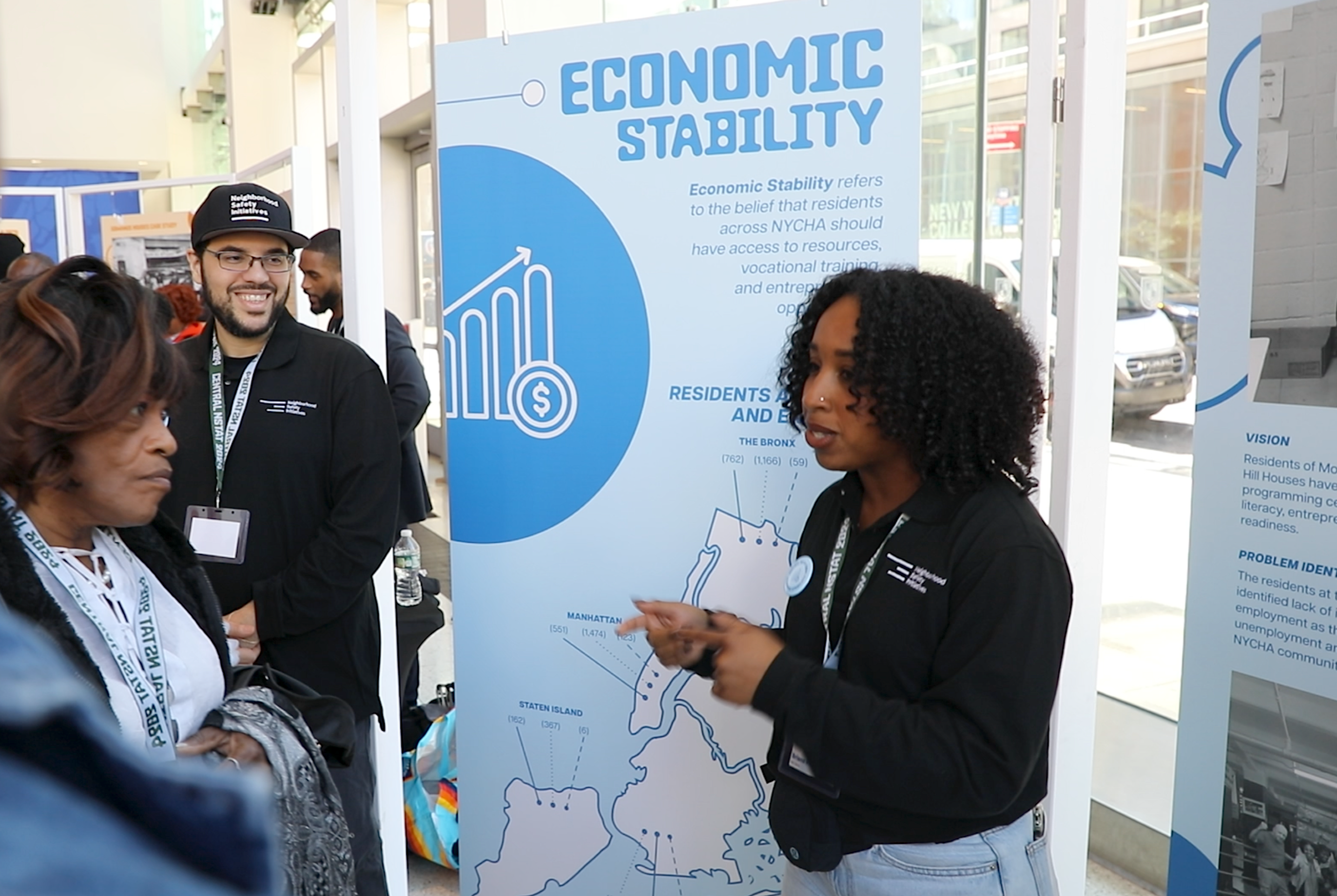Team member from Neighborhood Safety Initiatives displays a presentation board on economic stability at Community Policy Breakfast in Brooklyn.