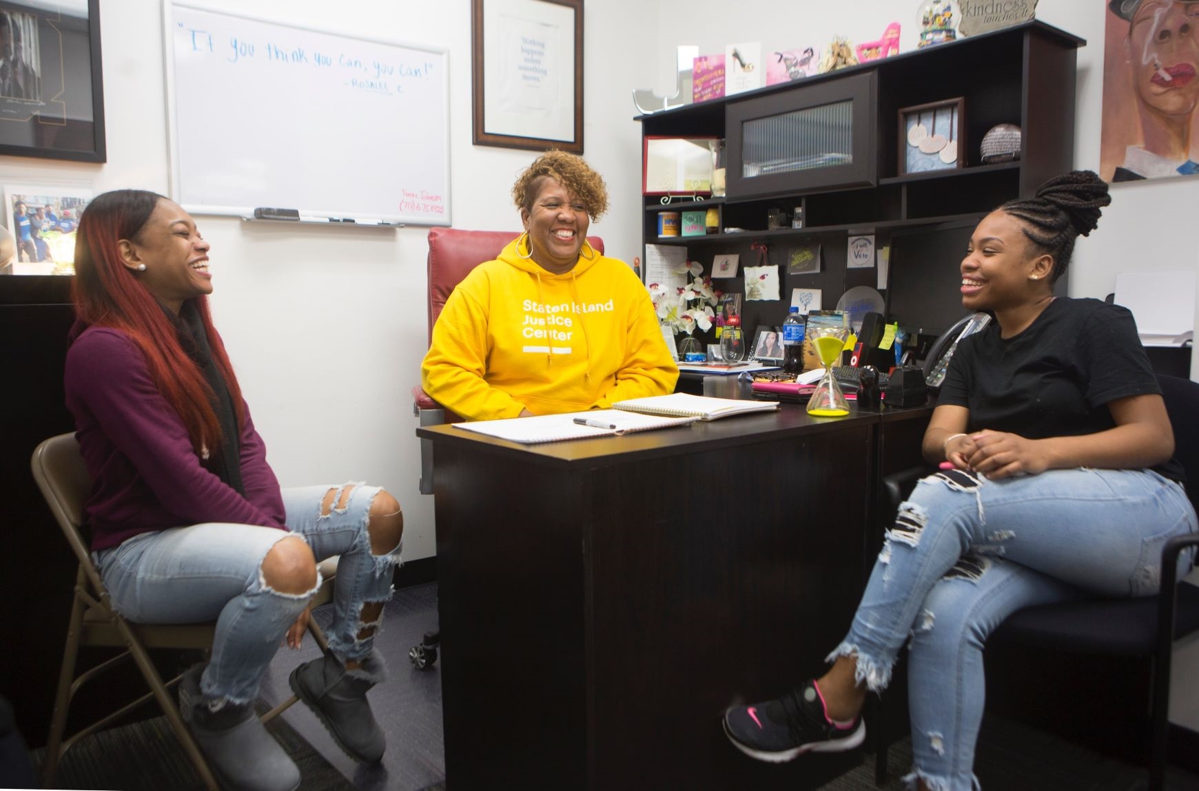 Three women sitting together around a desk, smiling and laughing together