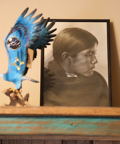 Framed portrait of Native youth alongside miniature bird carving.