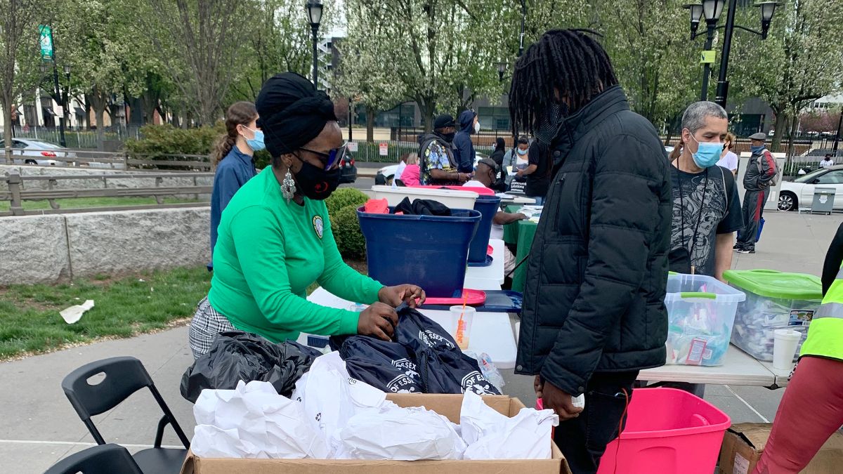 Staff member in a green shirt outside at a table handing out information and supplies to the community