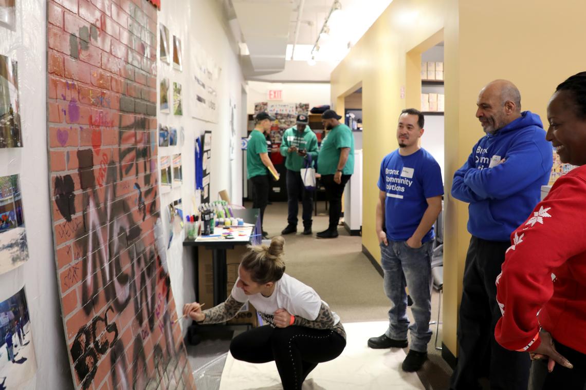 staff from various programs participating in an art activity in the office. Staff standing and talking while one draws on the graffiti wall.