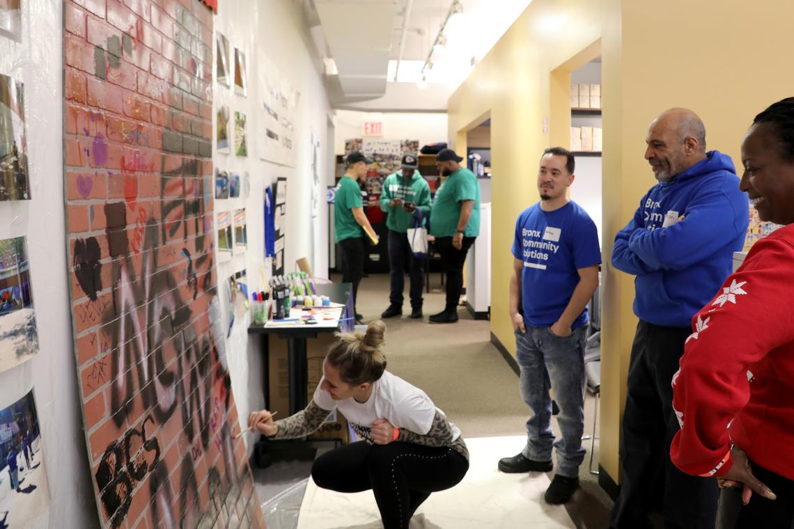 staff from various programs participating in an art activity in the office. Staff standing and talking while one draws on the graffiti wall. 