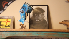 Framed portrait of Native youth alongside wooden bird miniature.
