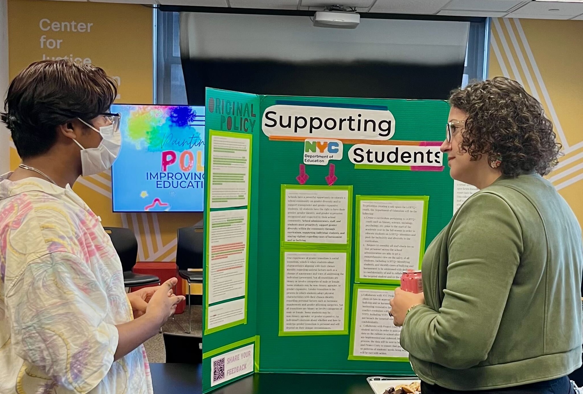 Two people, a Youth Fellow and a Center employee, speak at a poster board set up to display the young person's recommendations for schools