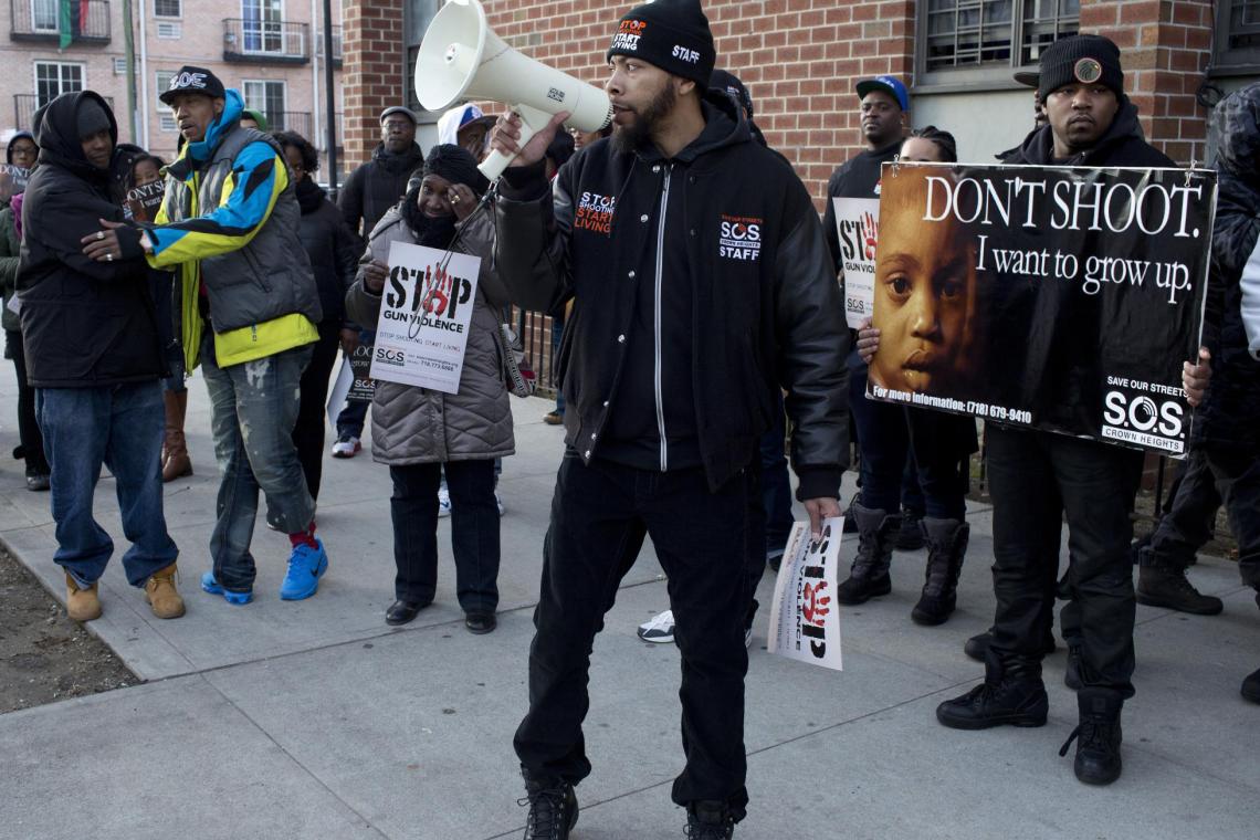 SOS Brooklyn staff holding banner and microphone, speaking to the community