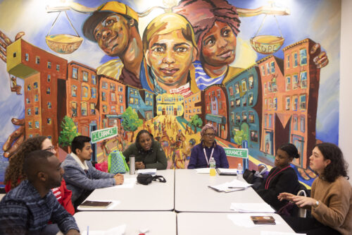 People around a table talking in front of a mural.