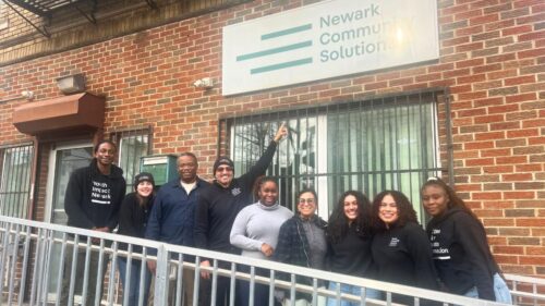 Group of people stand smiling outside of brick building underneath sign that says 