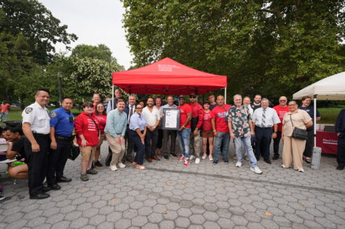 A group of people - including Red Hook Community Justice Center staff, children, and police officers - pose for a group photo with NYC Comptroller Brad Lander holding a commendation certificate.