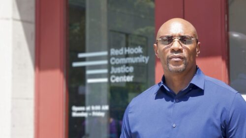 Close-up shot of Thaddeus Canty with blue button-down shirt and sunglasses standing at entrance to Red Hook Community Justice Center