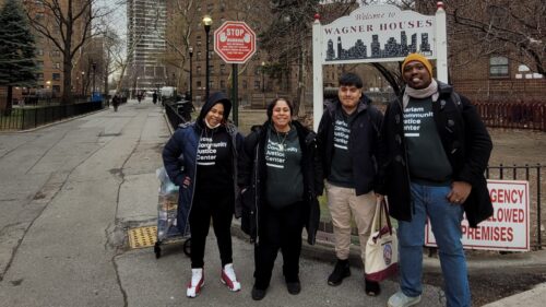 Four staff members in winter coats over Harlem Community Justice Center T-shirts stand outside the Wagner Houses in Harlem.