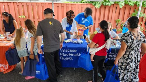 Parents with children stop at an outdoor table that reads 