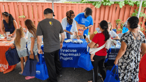 Parents with children stop at an outdoor table that reads 