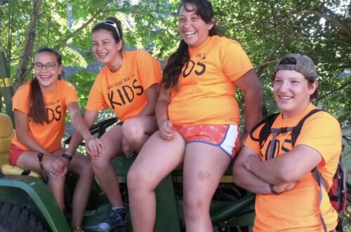 Four young people in orange t-shirts sit together, smiling.