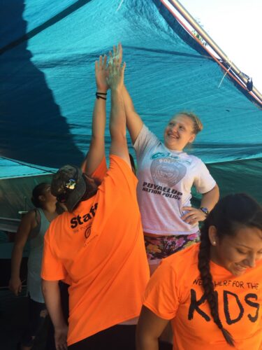 A young person in a white t-shirt high fives a staff member in an orange t-shirt.