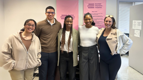 Five members of our Eviction Diversion Initiative team stand smiling for a photo indoors in front of wall posters with program name.