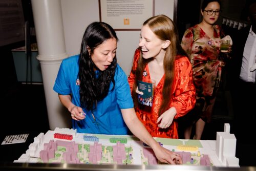 Two women, including Neighborhood Safety Initiatives Senior Director Layman Lee, speaking while interacting with a miniature architectural model of multiple apartment buildings.
