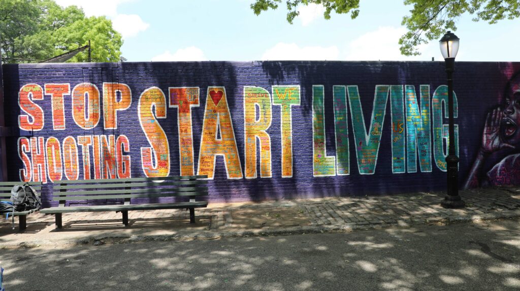 Outdoor mural featuring the words "Stop Shooting, Start Living" in large colorful font, with smaller text written within each letter
